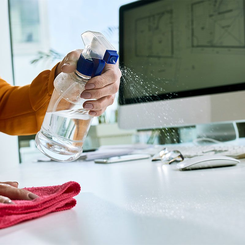 A person is cleaning a desk with a spray bottle.