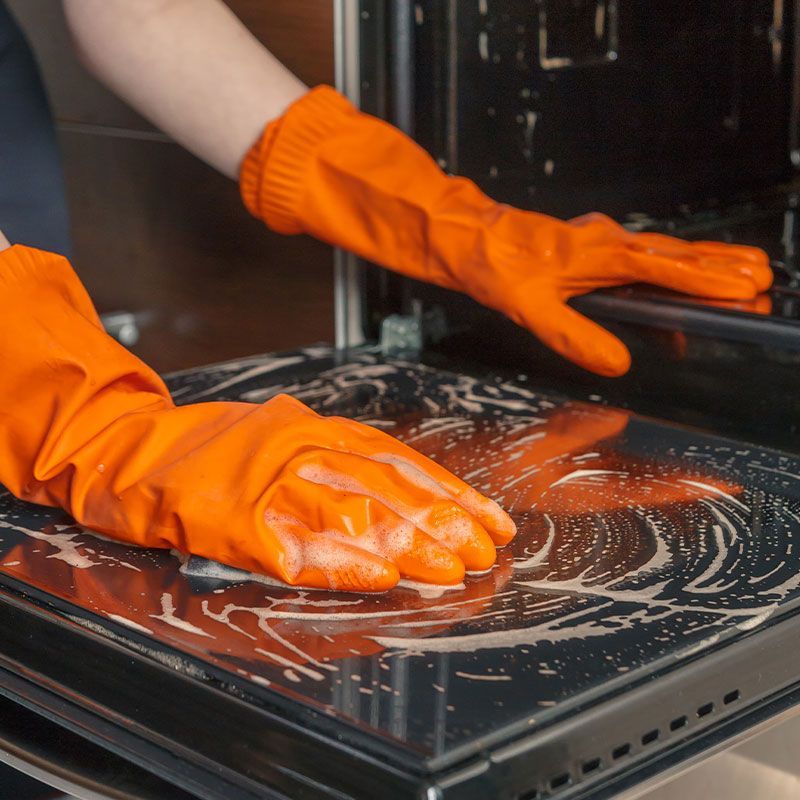 A person wearing orange gloves is cleaning an oven.