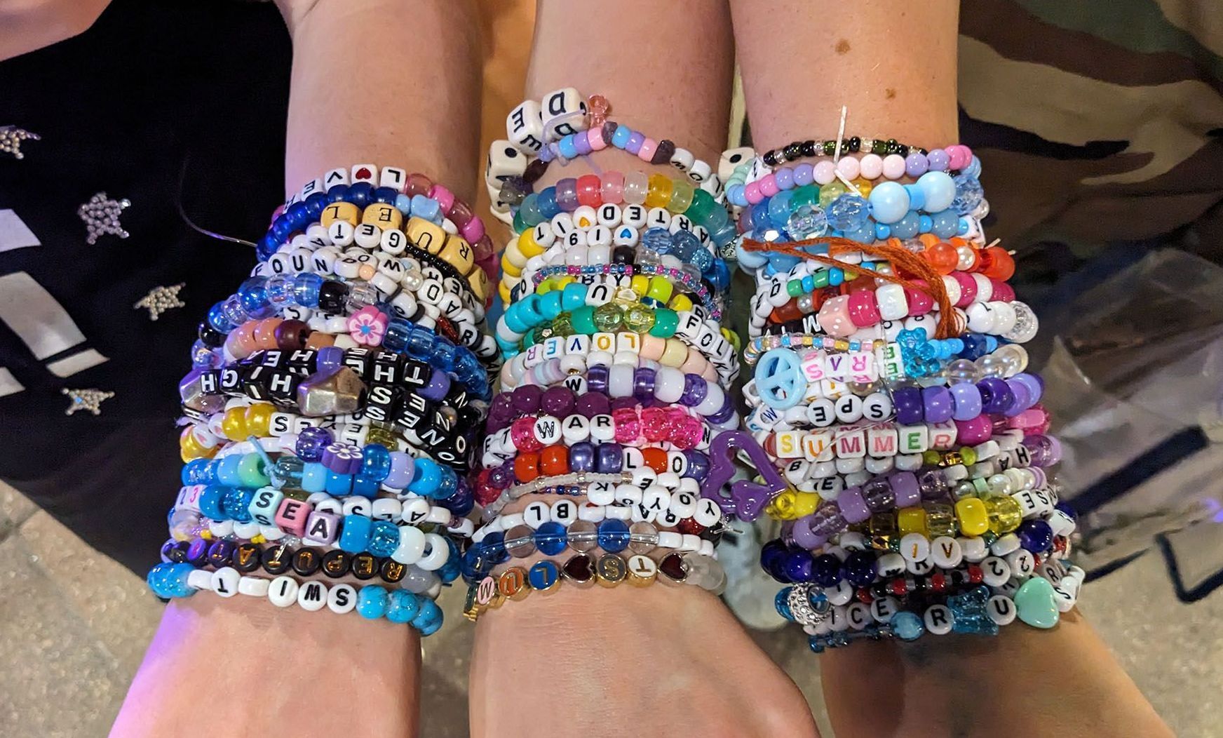 A color photo showing three wrists packed with friendship bracelets collected at one of Taylor Swift's Eras Tour shows.