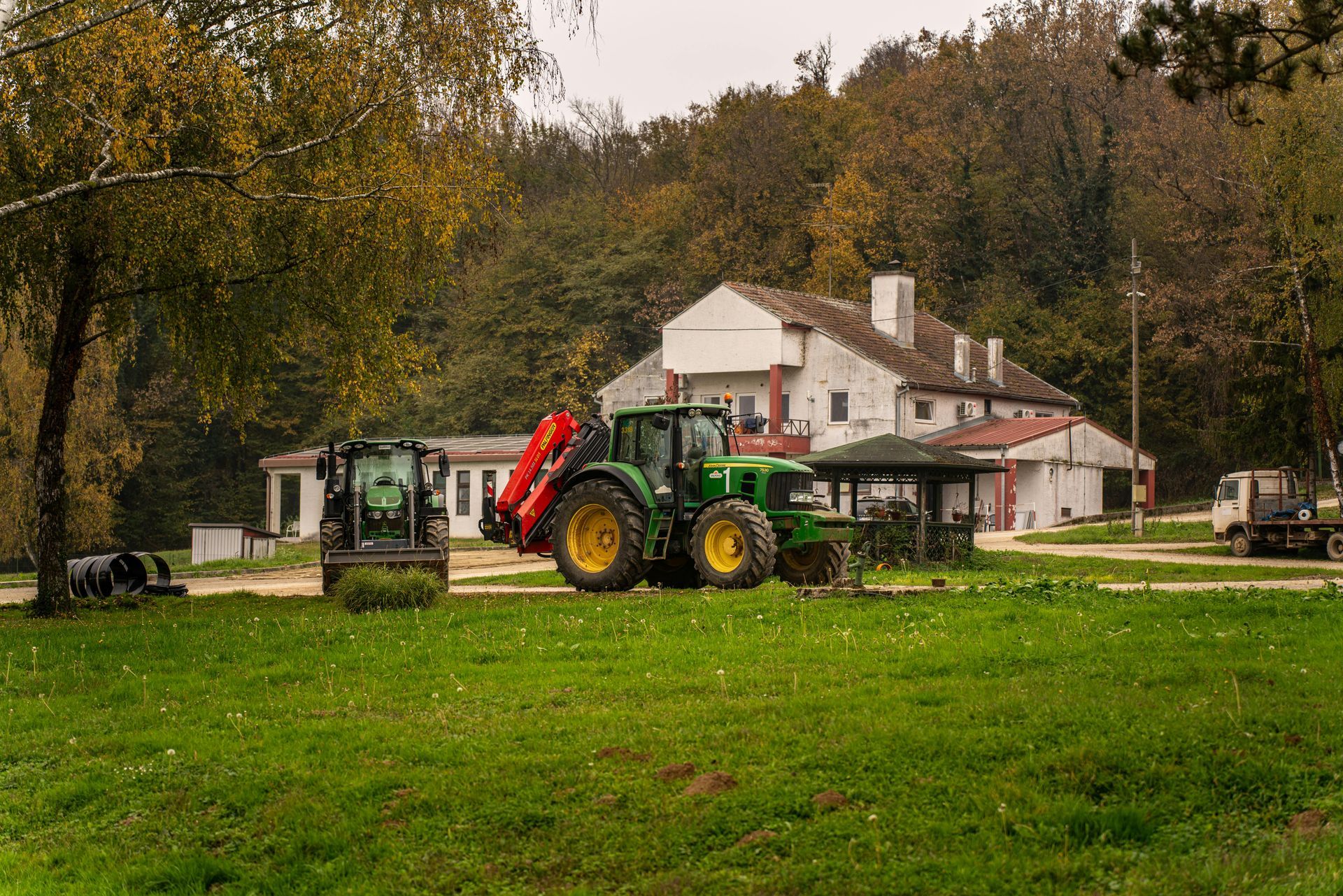 A green tractor is parked in a grassy field in front of a house.