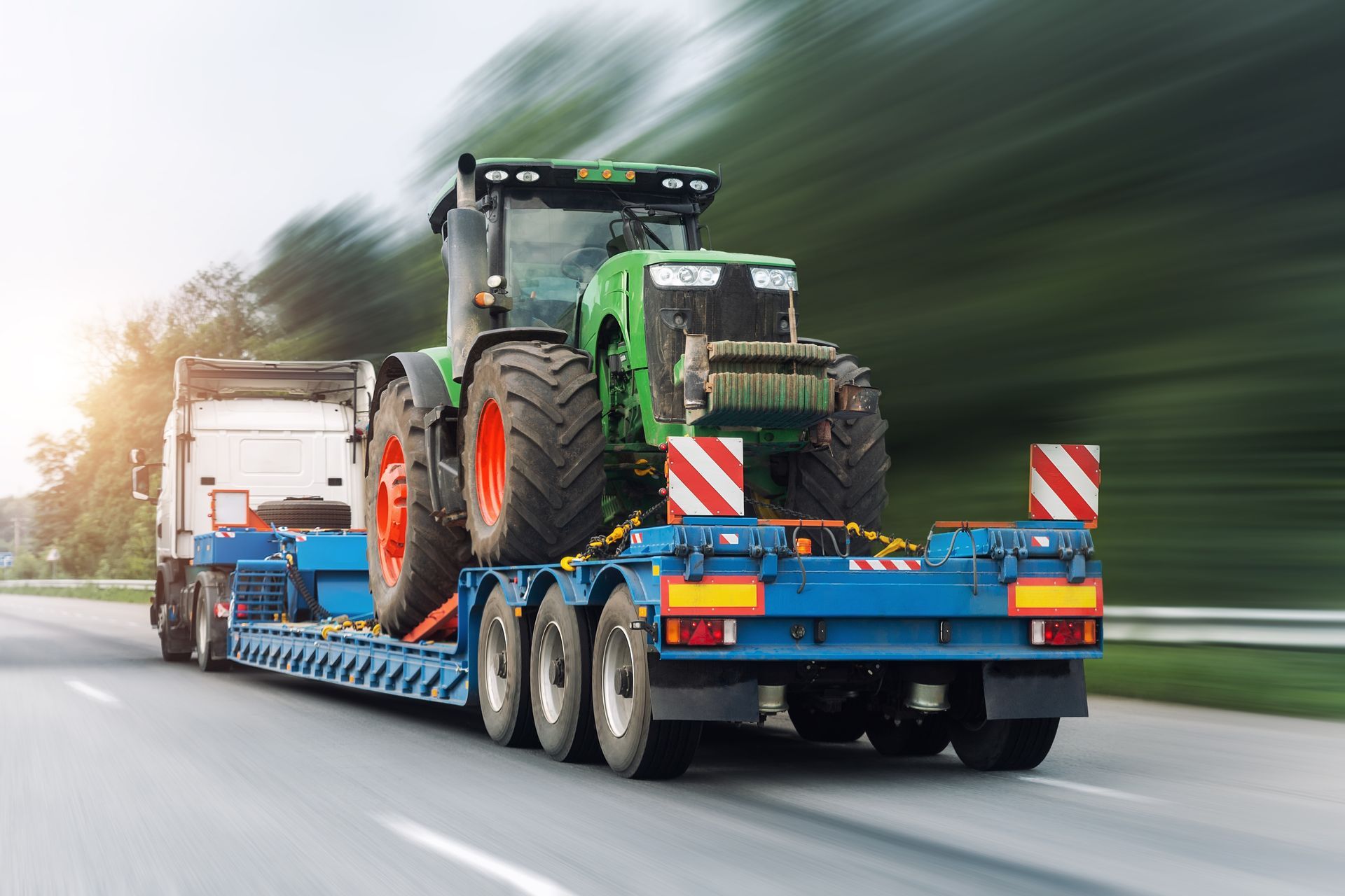 A tractor is being transported on a trailer on a highway.