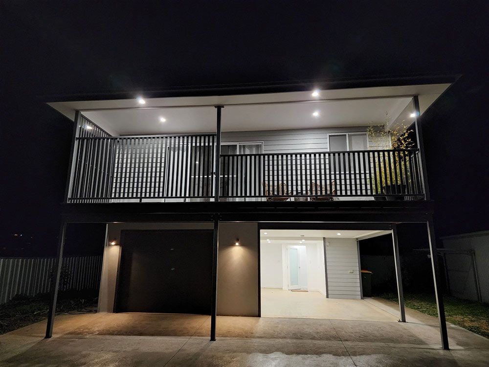 A House With A Balcony And A Garage Is Lit Up At Night — Chandolin Construction In Robin Hill, NSW