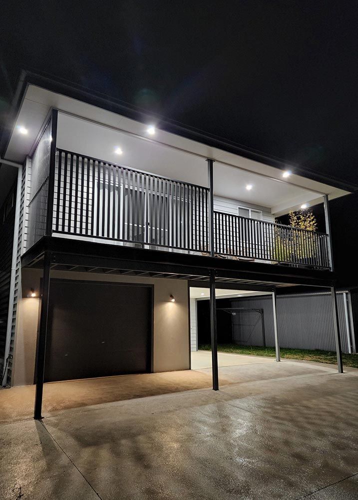 A House With A Balcony And A Garage Is Lit Up At Night — Chandolin Construction In Robin Hill, NSW