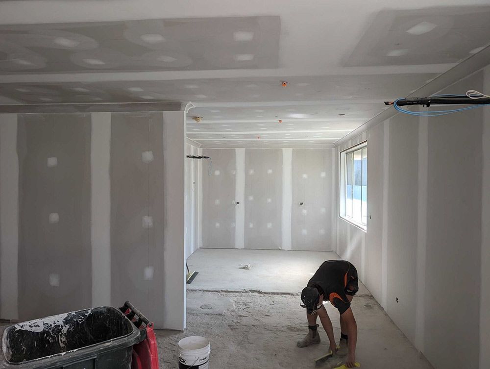 A Man Is Kneeling Down In A Room With Drywall On The Walls — Chandolin Construction In Robin Hill, NSW