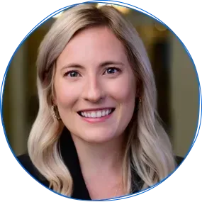Man with short, gray hair smiles wearing a blue blazer and button-down shirt outdoors.