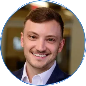 Man in a blue suit smiling at the camera; blue circle framing the portrait.