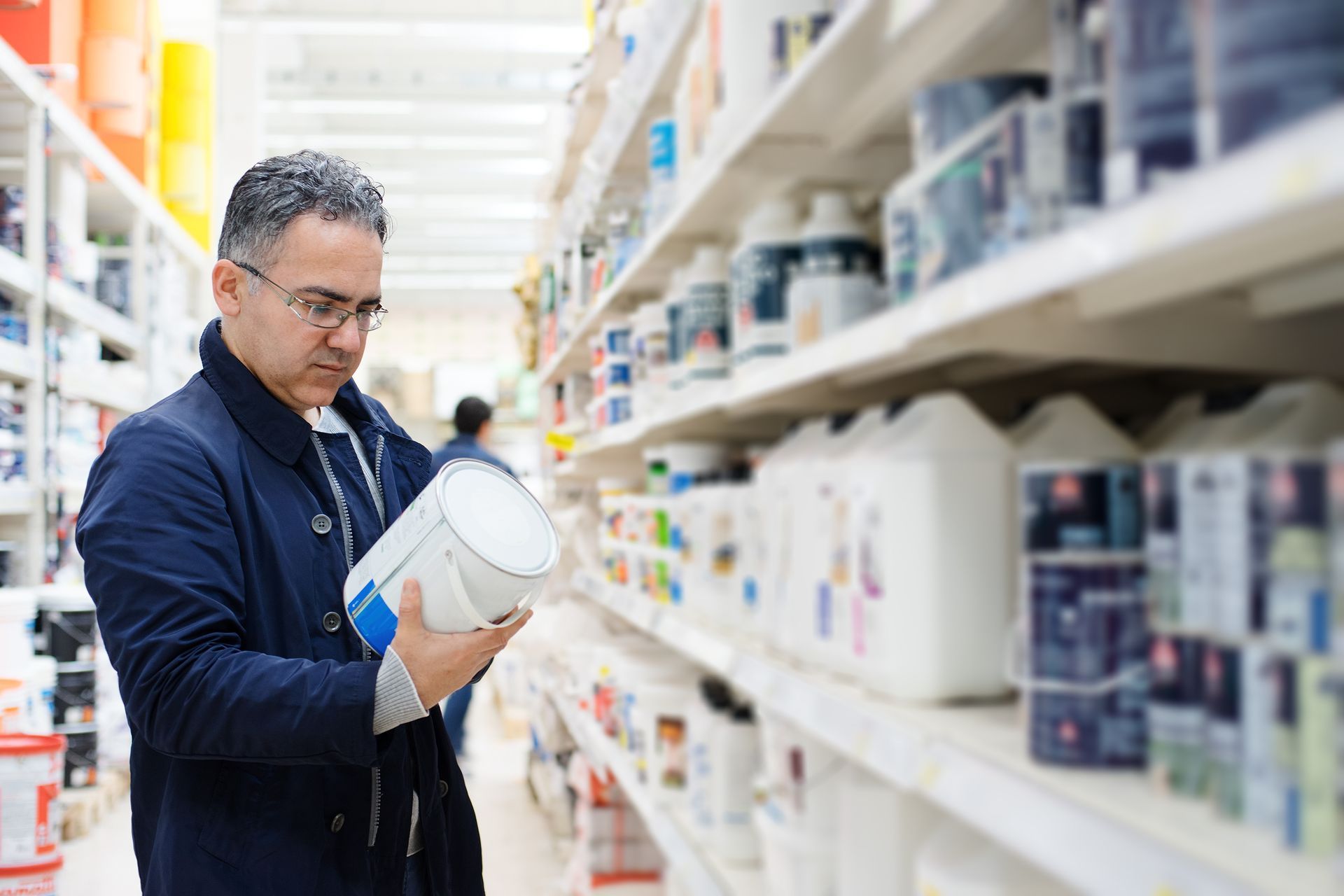 Man selecting paint colors from shelves in a hardware store aisle.