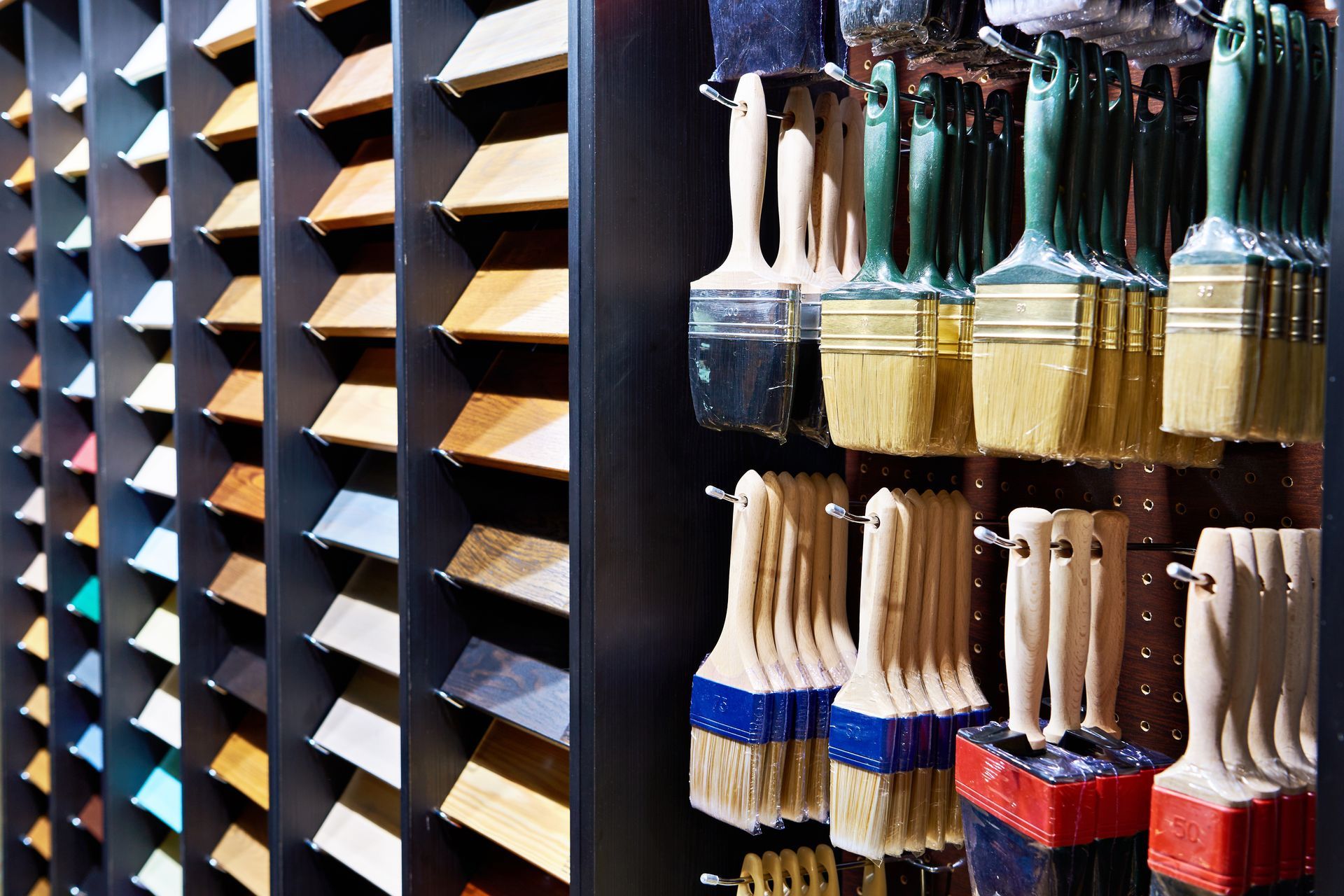 Paintbrushes hanging beside wood finish samples display in a hardware store.