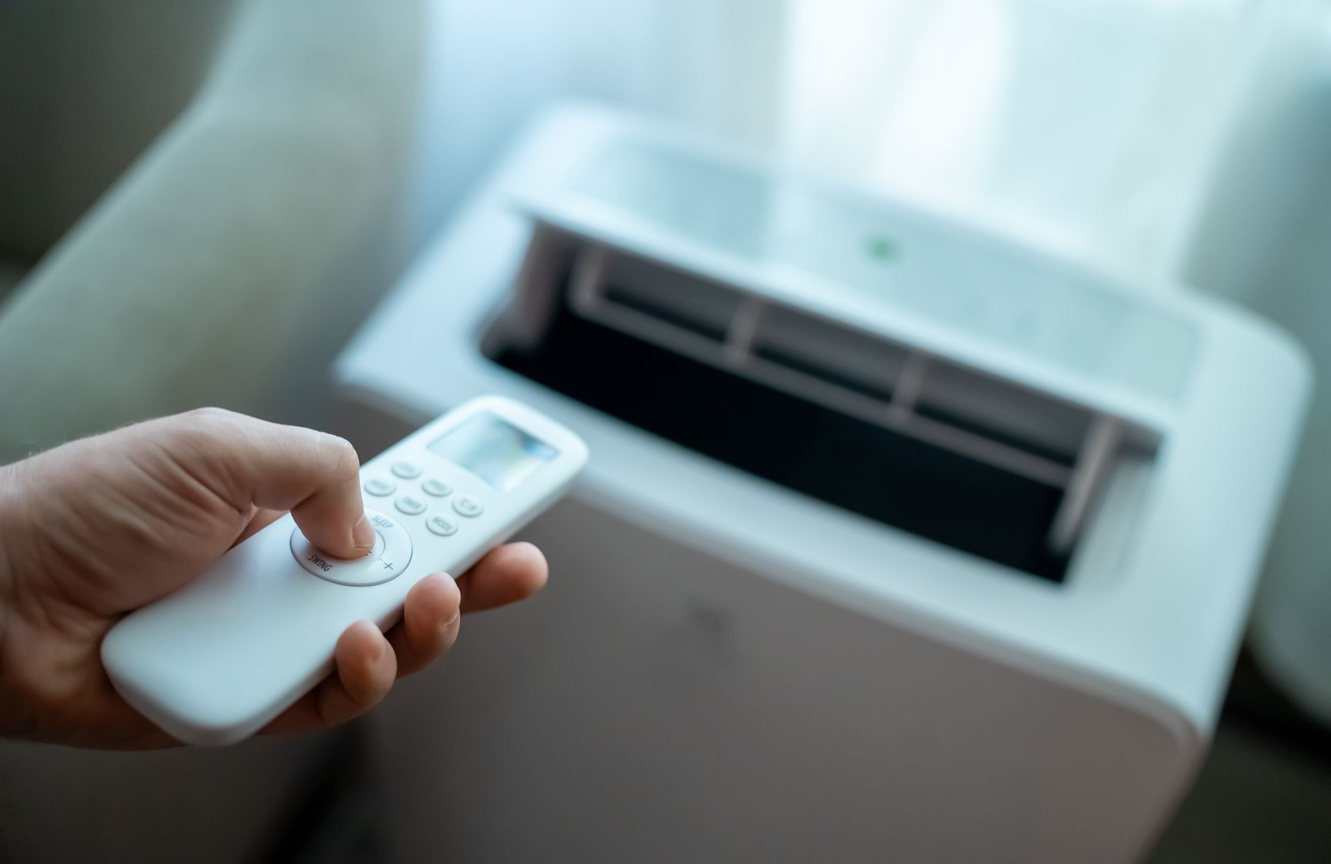 Hand holding remote control aimed at portable air conditioner unit. Hand holding remote control aimed at portable air conditioner unit.