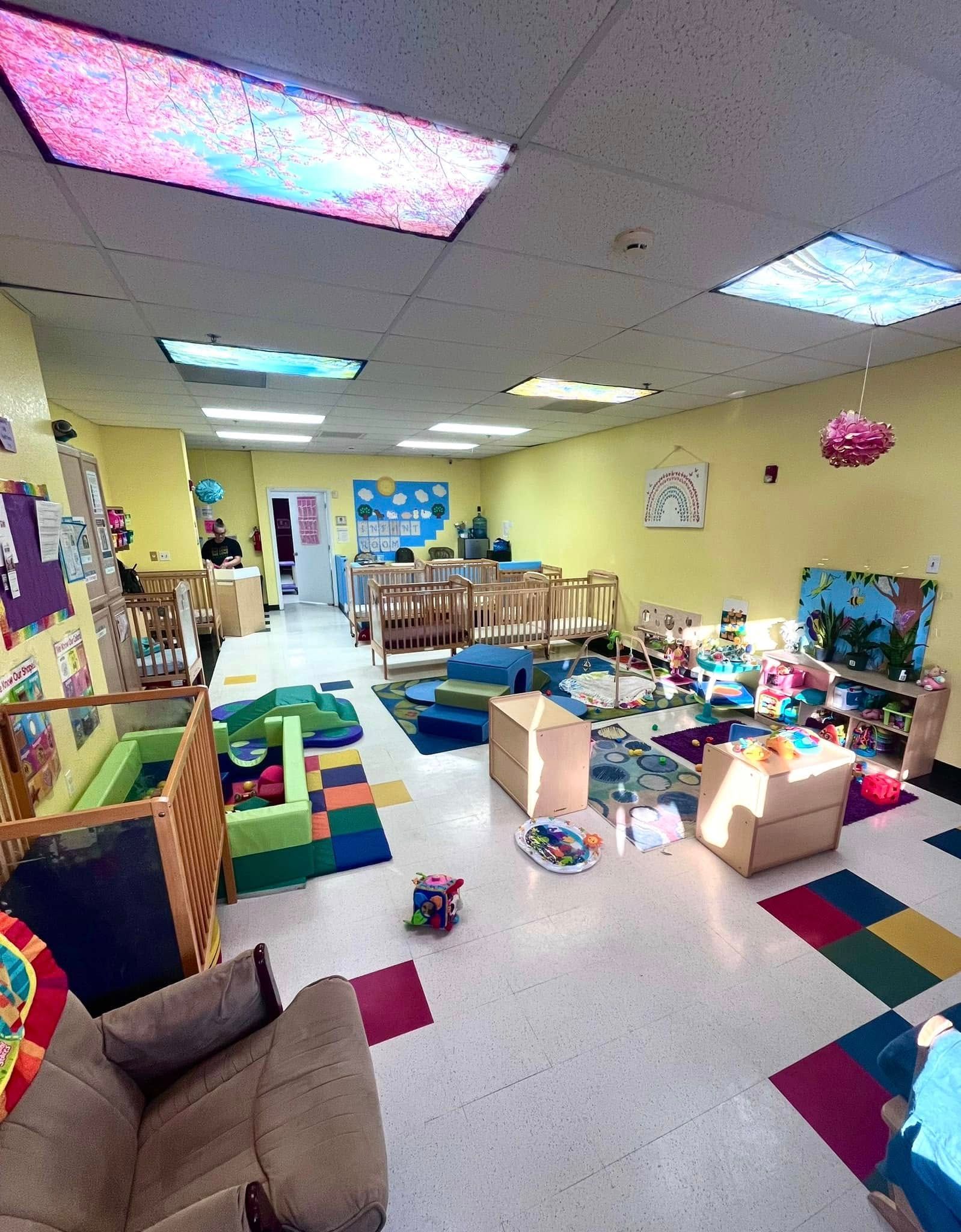 Daycare room: Cribs, toys, colorful mats, and a small sofa on yellow walls.