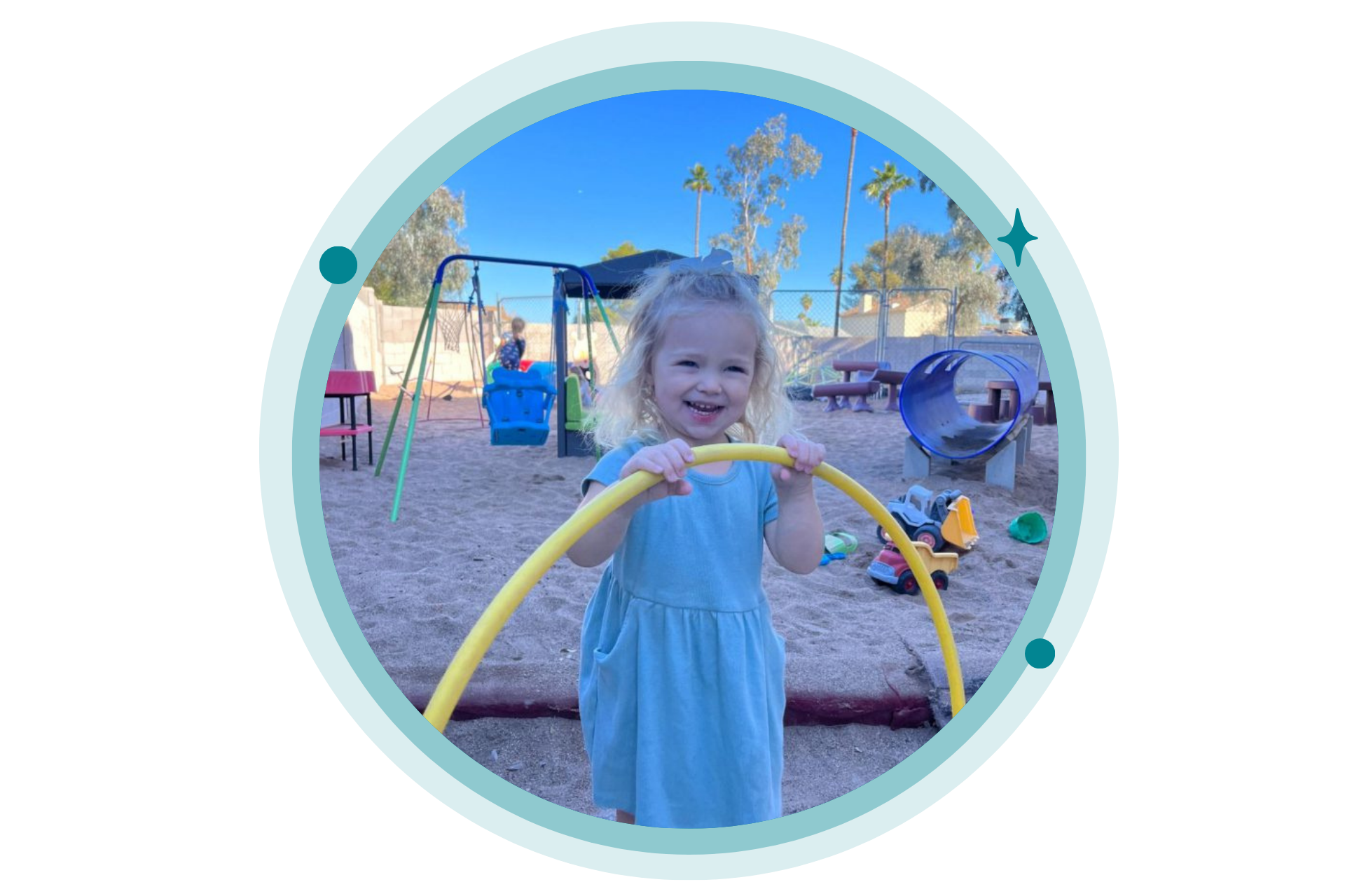 Child at a playground holding a yellow hula hoop, smiling.