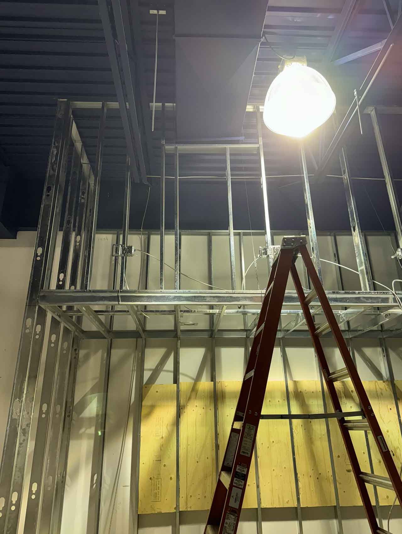 Une échelle est posée sous une lumière dans un bâtiment en construction.