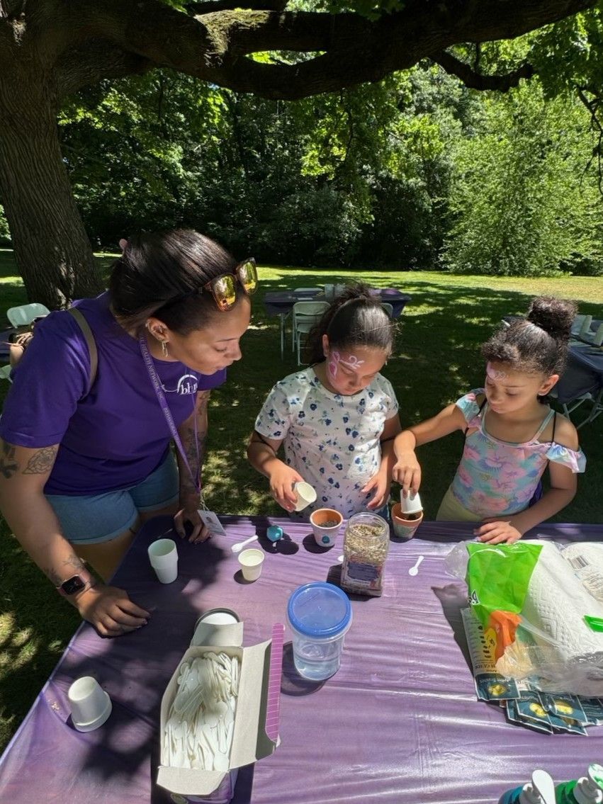 A BHN staff member shows two children how to put seeds into the terracotta pots that they painted.