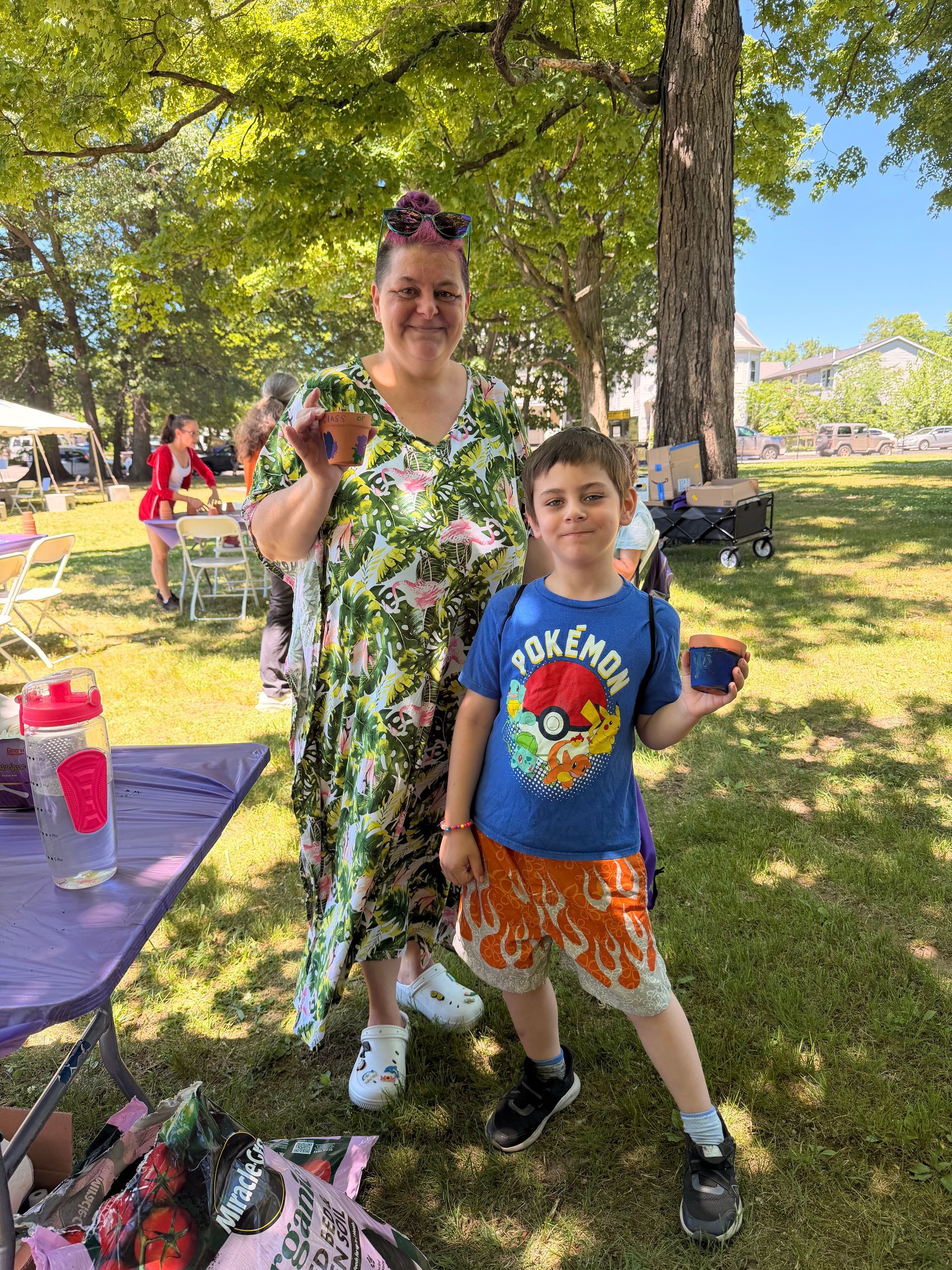 A woman and child standing in the park posing to show off the terracotta pots that they painted.