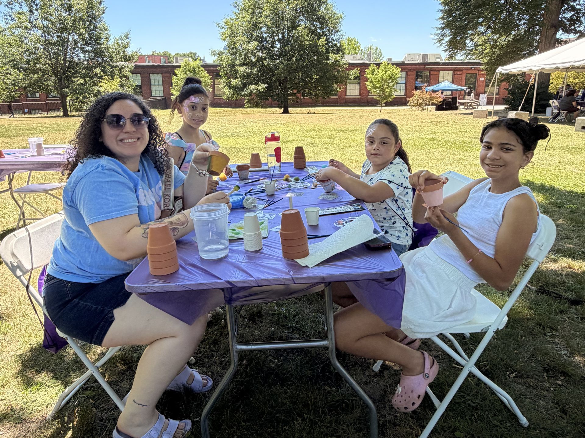 A woman and three children smile for a photo while painting small terracotta pots at BHN's mental health awareness community event in Gurdon Bill Park.