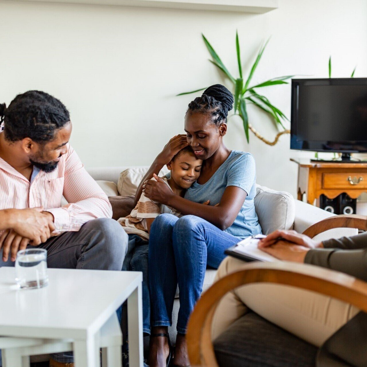 People chatting in a bright living room, sitting on a sofa and chairs around a coffee table.
