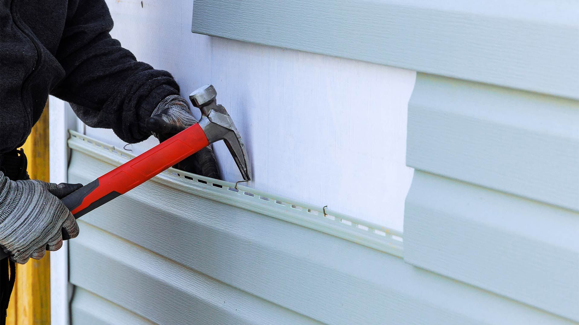 A man is installing siding on a house with a hammer.