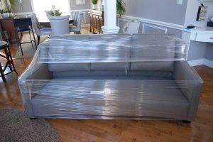 A couch is wrapped in plastic wrap in a living room.