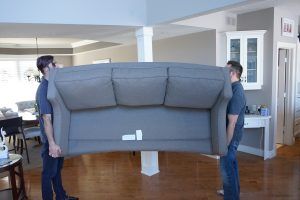 Two men are carrying a couch in a living room.