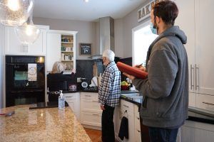 A man is standing in a kitchen talking to an older man.
