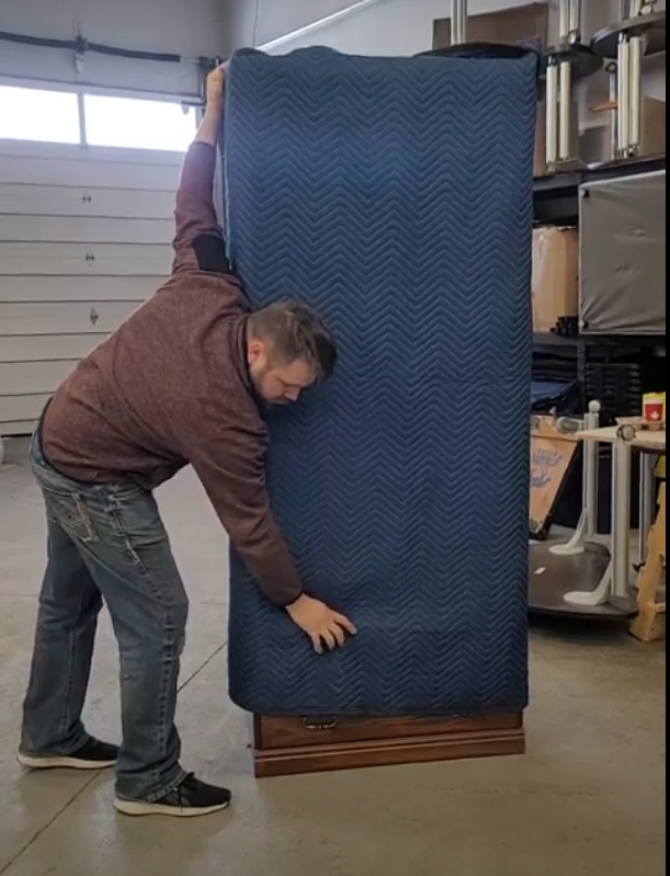 A man is holding a blue blanket over a large piece of furniture.