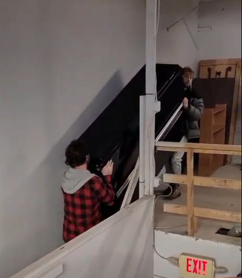 A man is carrying a piano up a set of stairs next to an exit sign
