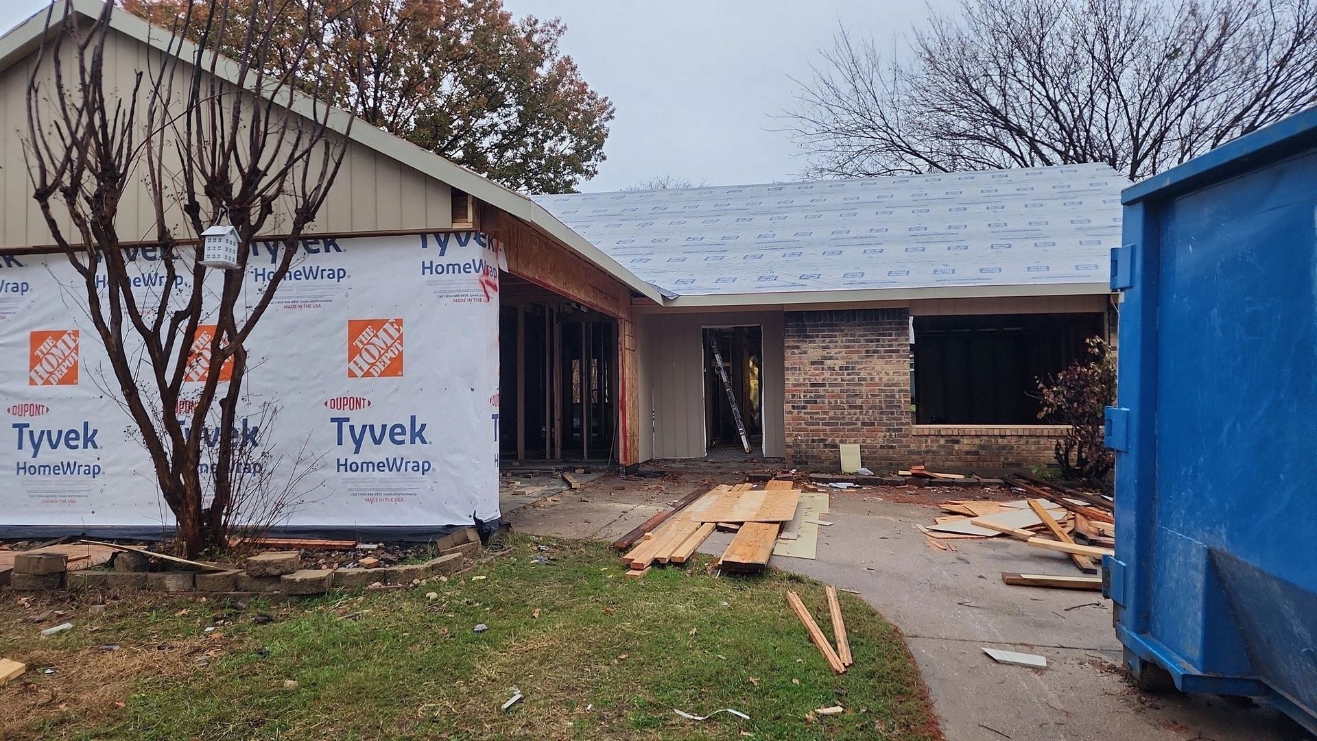 A house under construction with a blue dumpster in front of it.