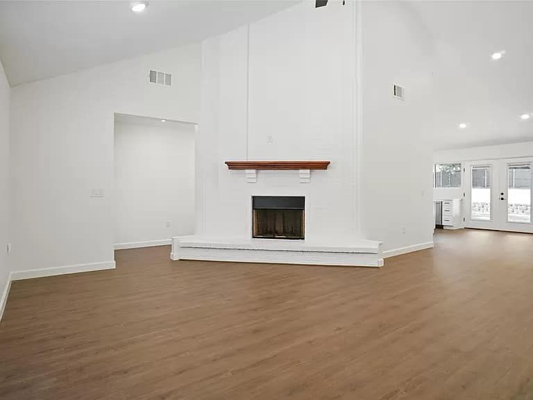 An empty living room with a fireplace and hardwood floors.