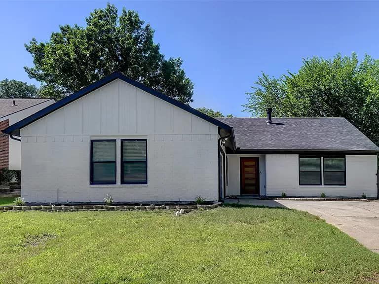 A white house with a black roof is sitting on top of a lush green lawn.