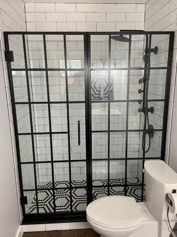 A bathroom with a toilet , shower , and black shower door.