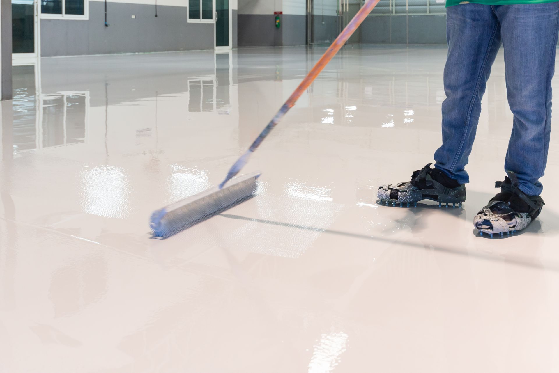 A person is cleaning a concrete floor with a broom.