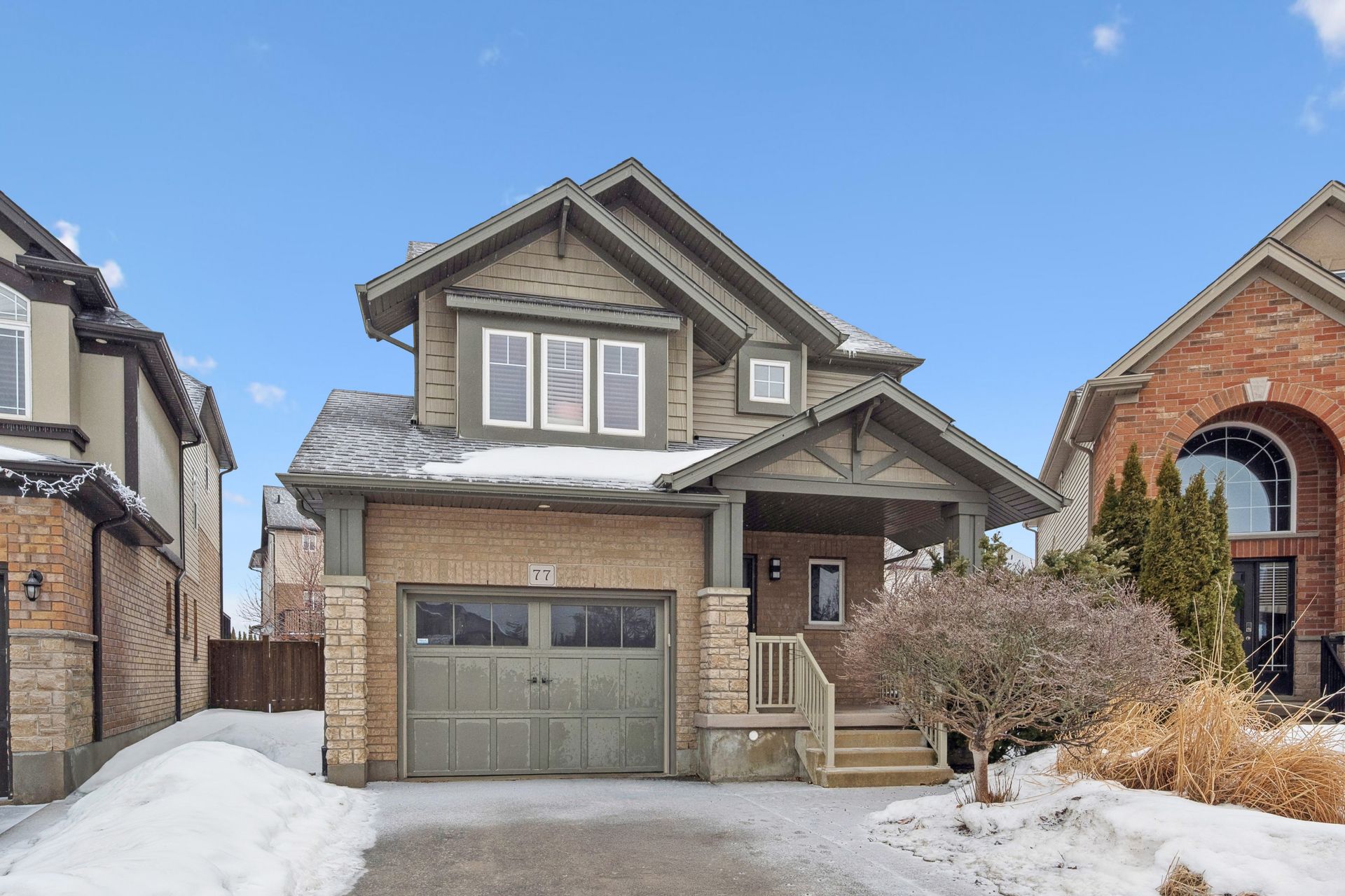 Two-story house with green garage door, brick facade, snow-covered yard, and clear sky.
