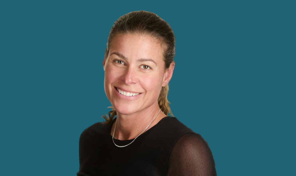 A woman in a black shirt is smiling for the camera against a blue background.