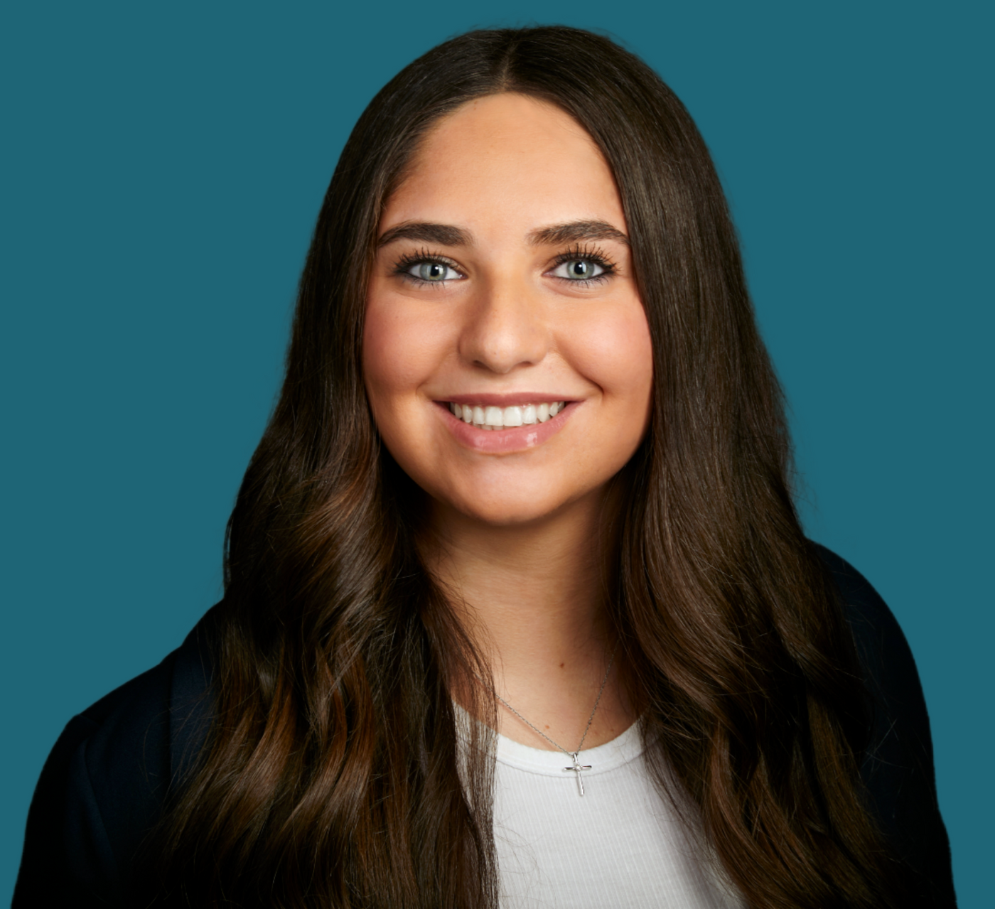 A woman with long brown hair is smiling in front of a blue background.