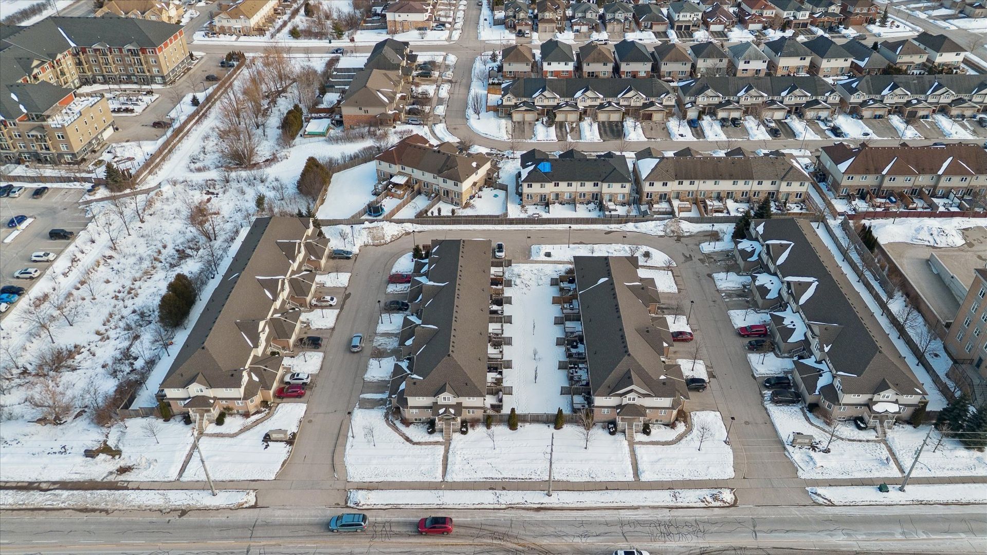 Aerial view of snow-covered suburban townhouses and streets, viewed from above.