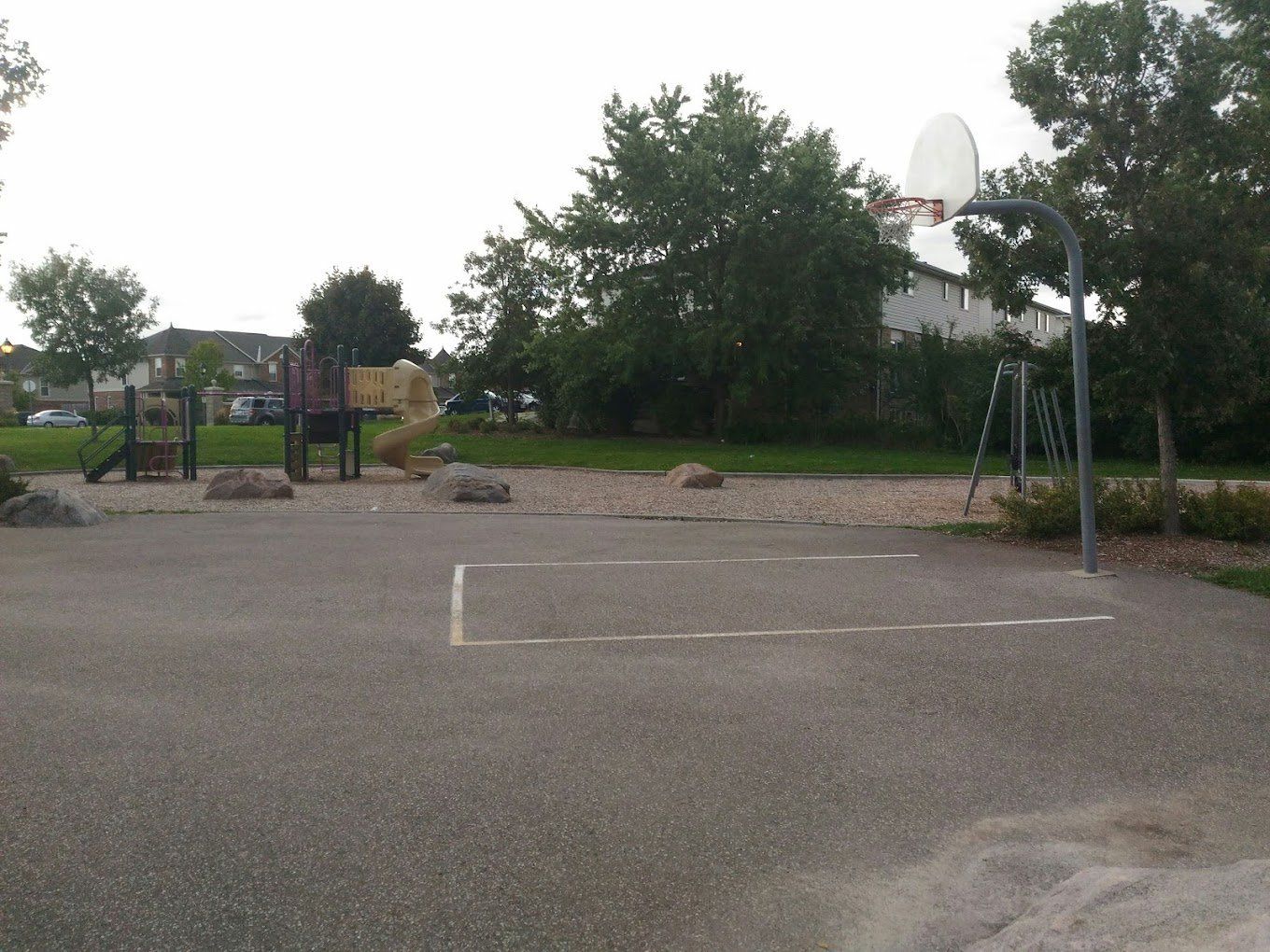 A basketball court in a park with a playground in the background