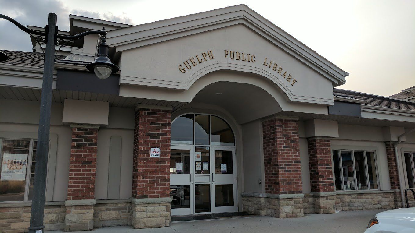 A white car is parked in front of a public library.