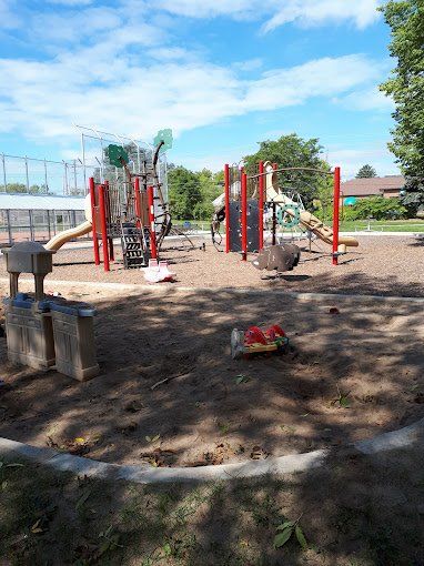 A playground with a bird sitting in the dirt in front of it.
