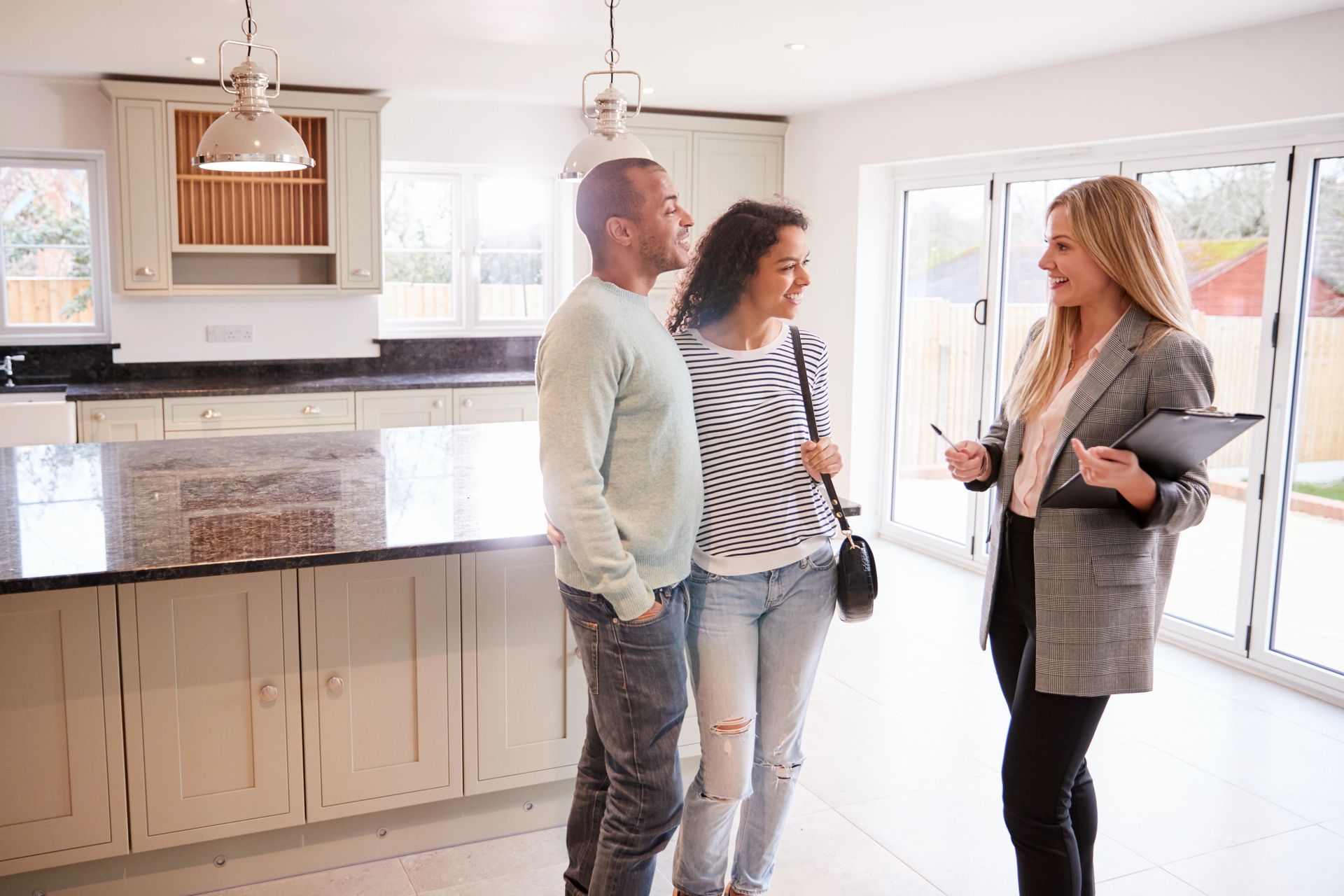 Couple touring a kitchen with a real estate agent; agent points and holds clipboard.