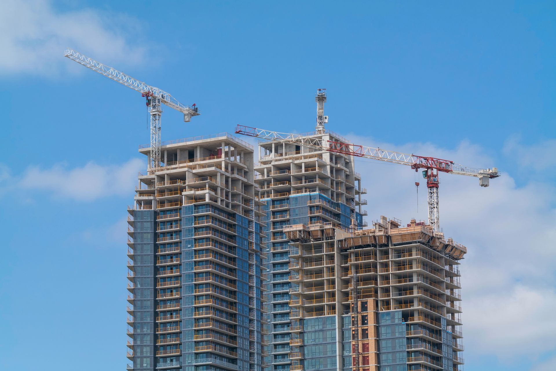 Skyscrapers under construction with several cranes against a blue sky.