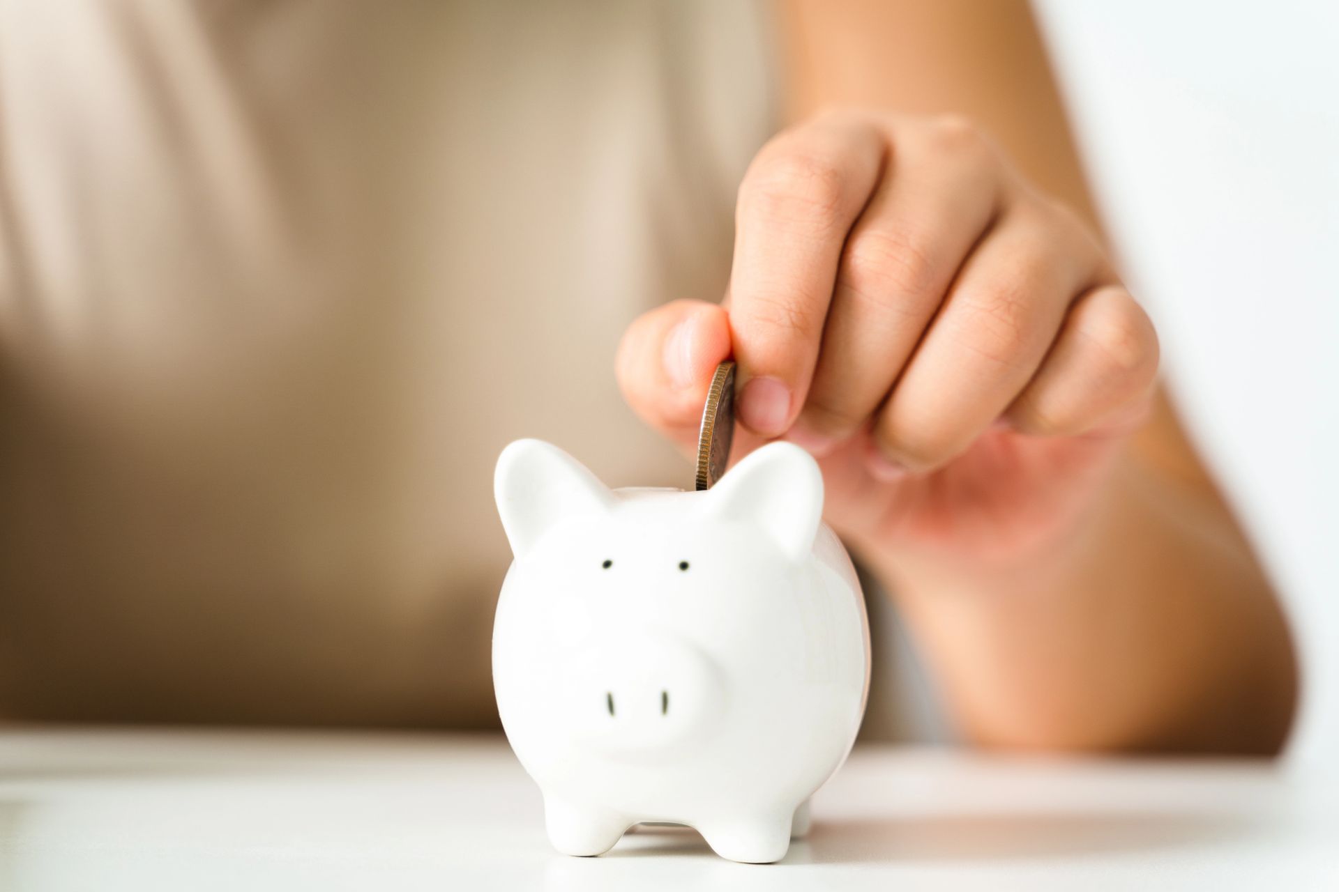 Hand placing a coin into a white piggy bank on a table