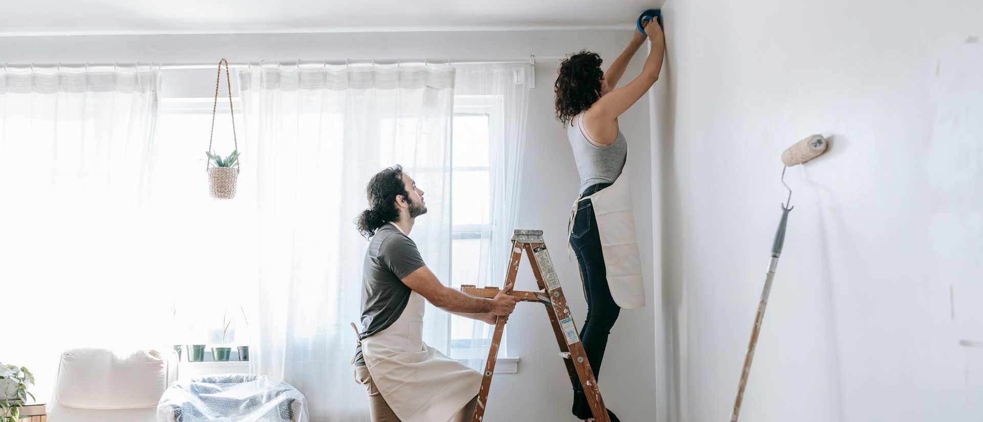 A man and a woman are painting a wall in a living room.