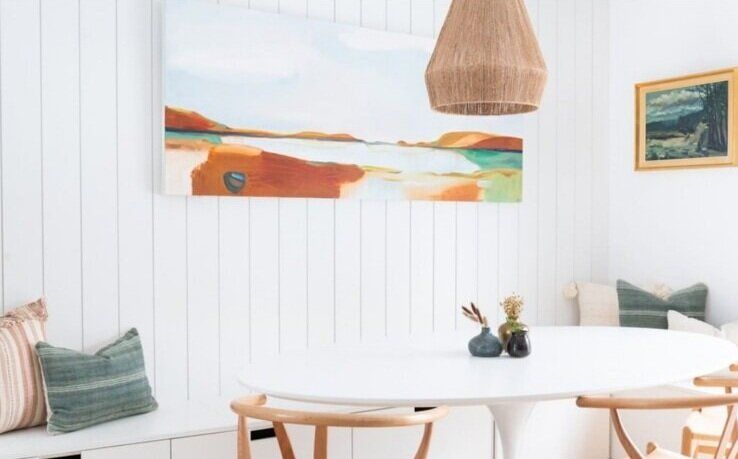 A dining room with a table and chairs and a painting on the wall.
