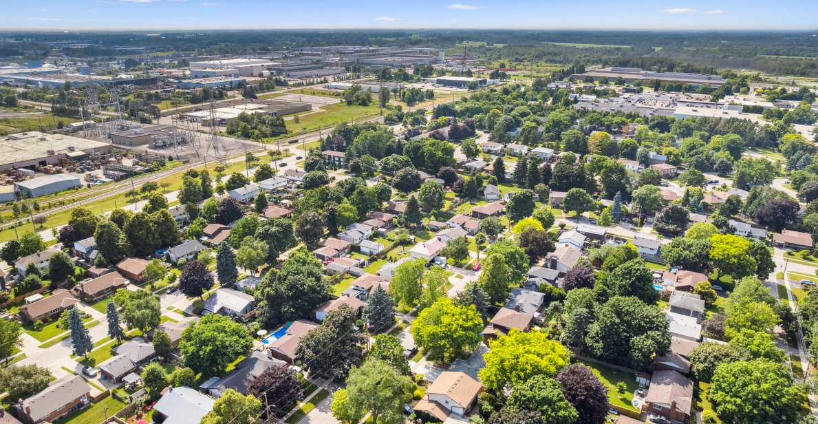 Aerial view of a residential neighbourhood with many trees, houses, and a distant industrial area on