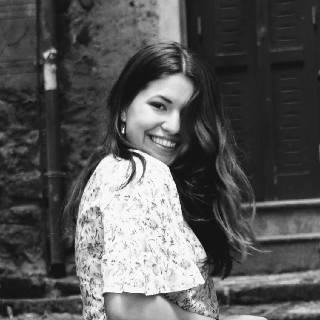 A black and white photo of a woman smiling in front of a building.