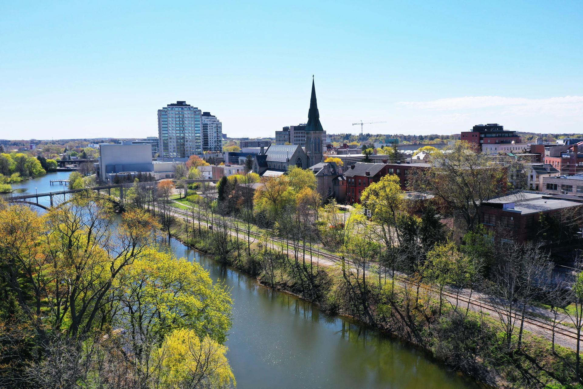 Cityscape with river, trees, buildings, including a tall church spire and a modern glass building.