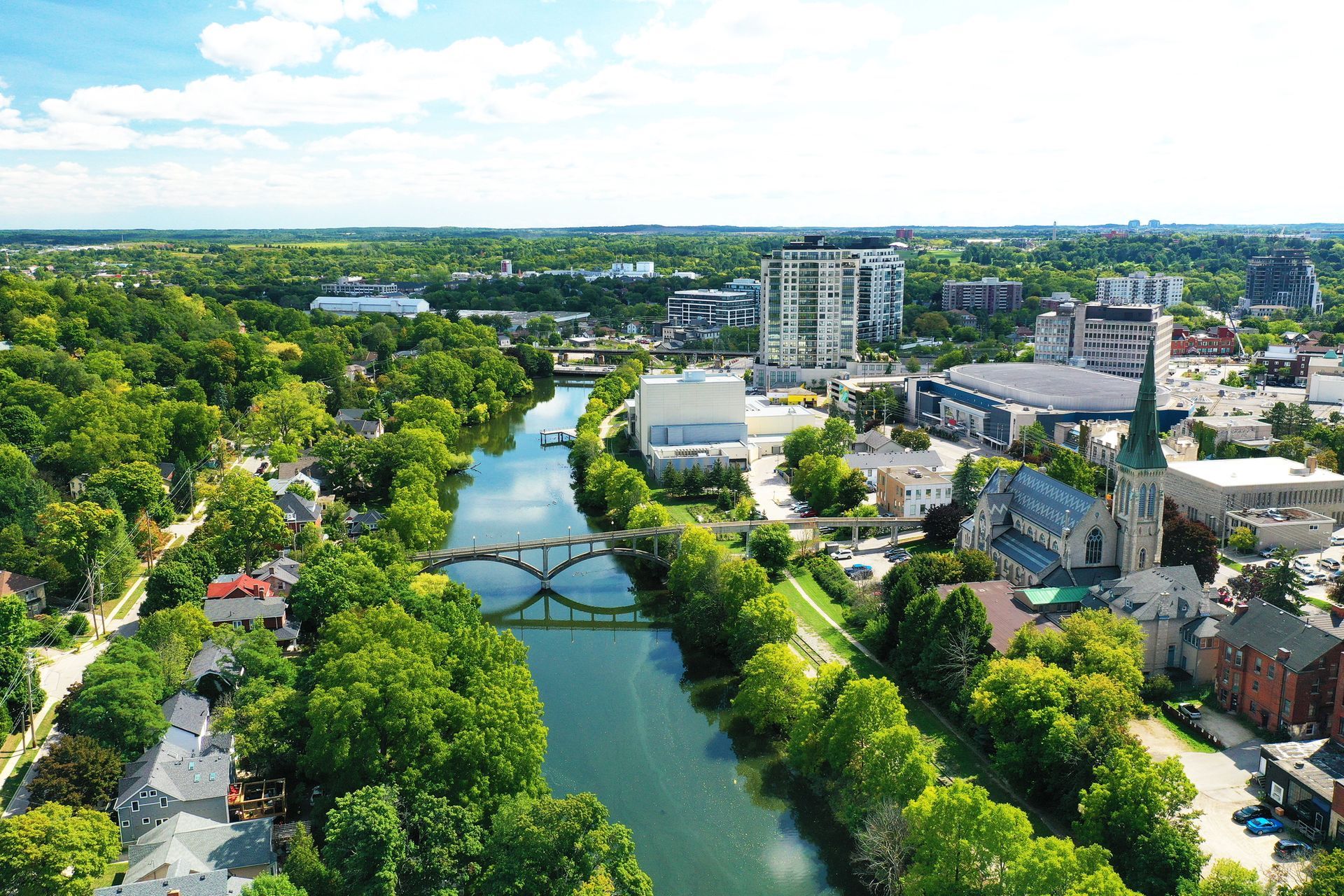 Aerial view of Guelph with a river, bridge, and tall buildings surrounded by trees.