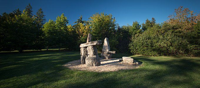 There is a statue in the middle of a grassy field in the middle of a forest.