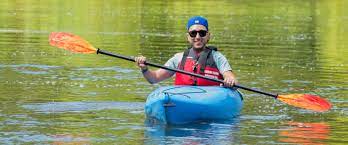 A man is paddling a blue kayak on a lake.