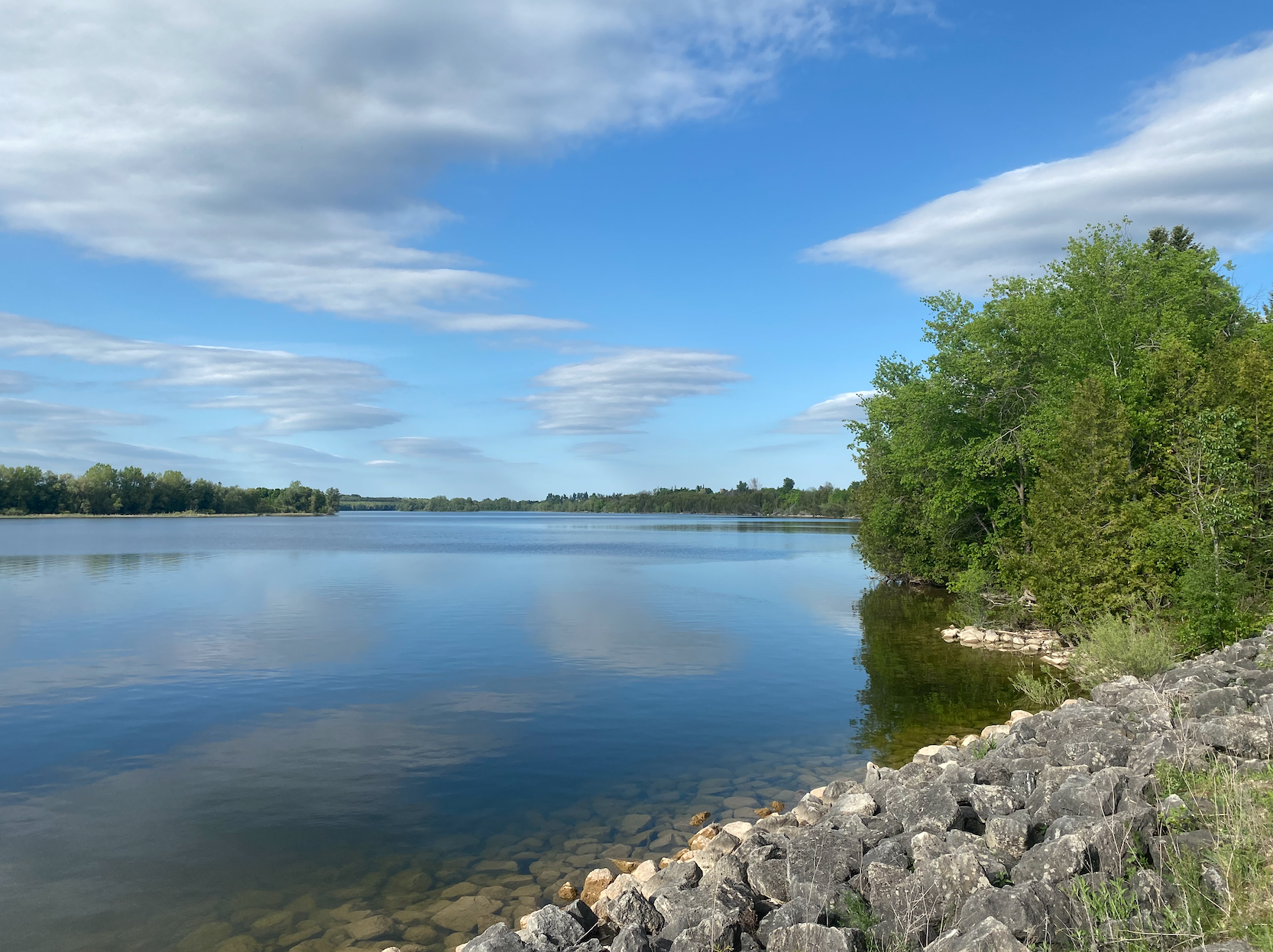 A large body of water surrounded by trees and rocks on a sunny day.